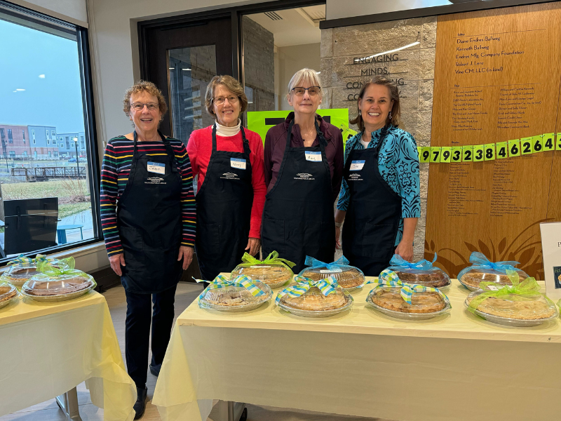 Four smiling people standing behind a table of pies