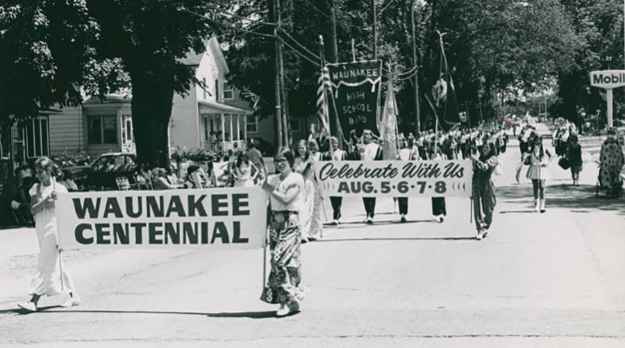 Waunakee Centennial Parade black and white historical image showing people marching with banners